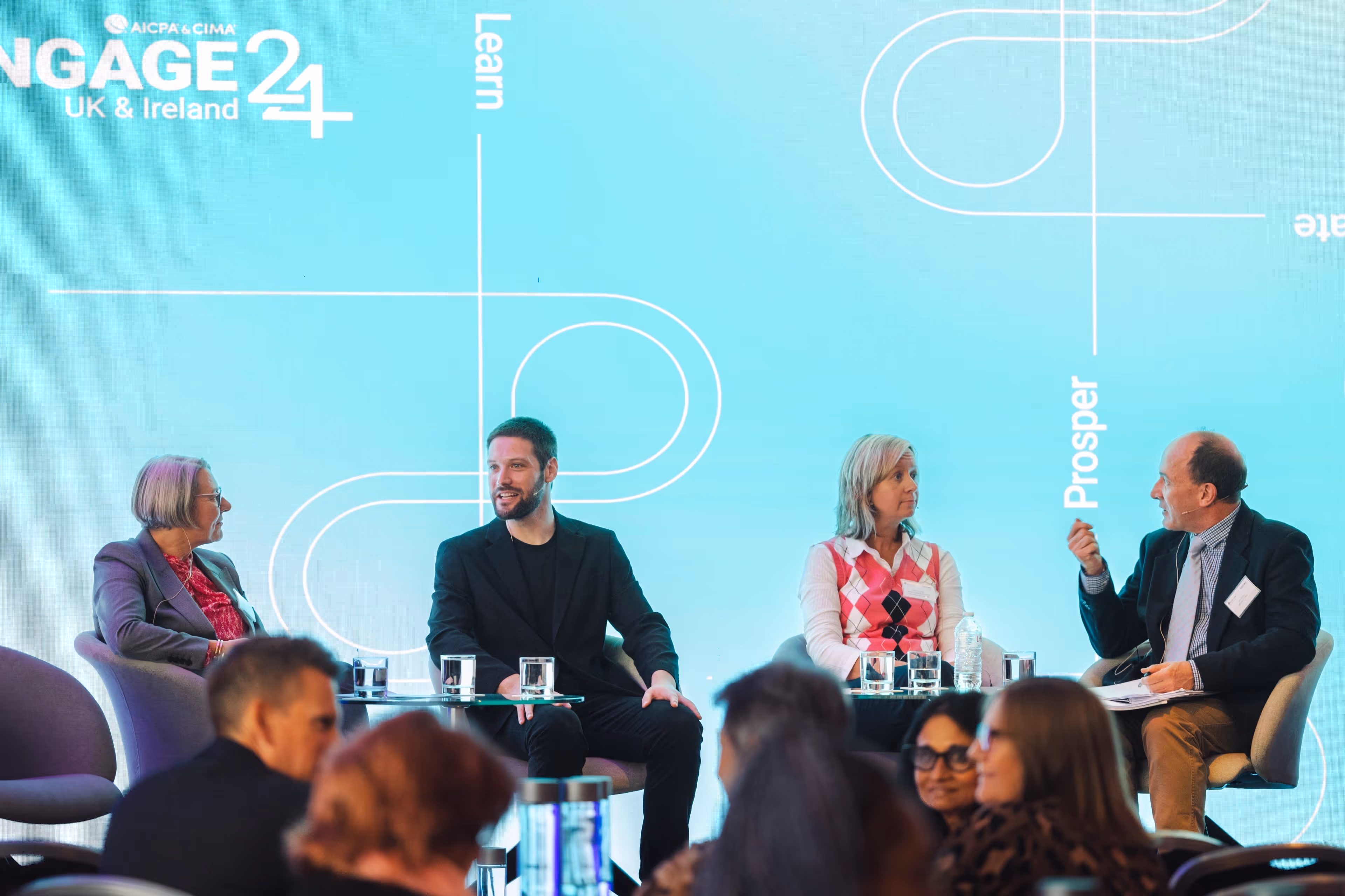 Four professional speakers sitting on stage during a panel discussion at the ENGAGE 24 conference with a bright blue backdrop and an audience in the foreground.