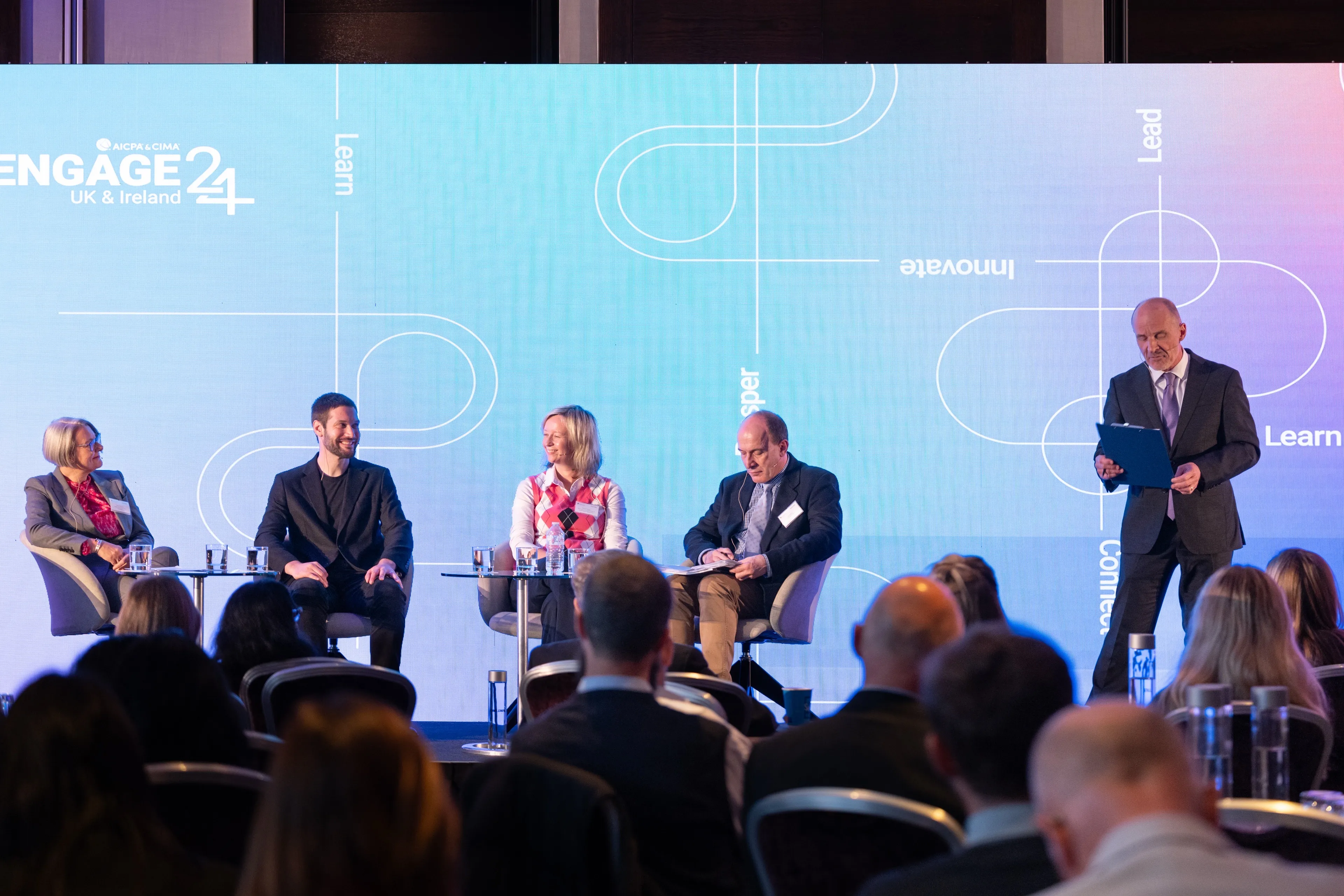 A panel discussion on stage at the ENGAGE 24 UK & Ireland conference, featuring four seated panelists, one standing moderator, and an attentive audience in the foreground.