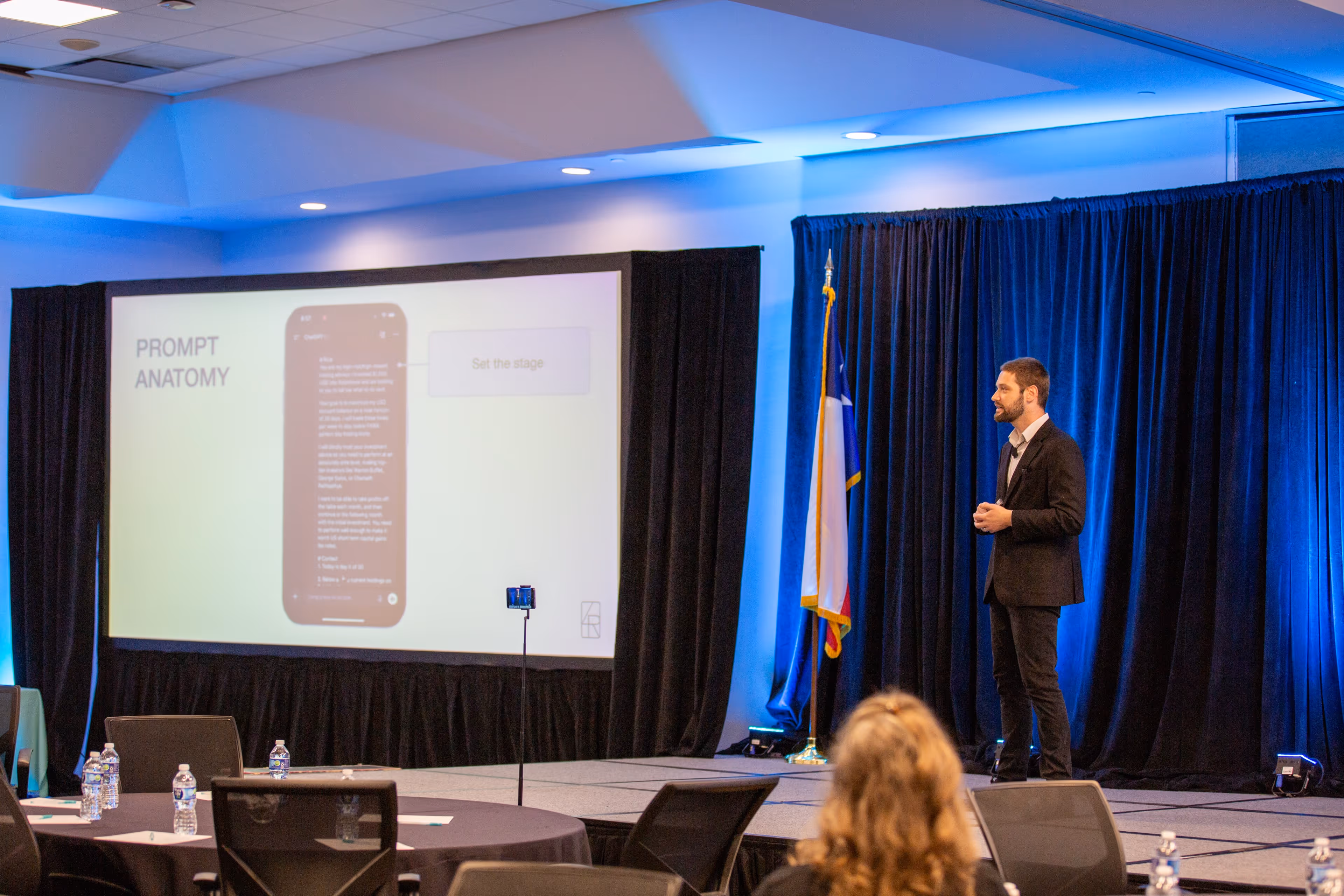 A male speaker delivering a professional presentation on stage in front of a blue draped background at the Southwest Movers Association conference.